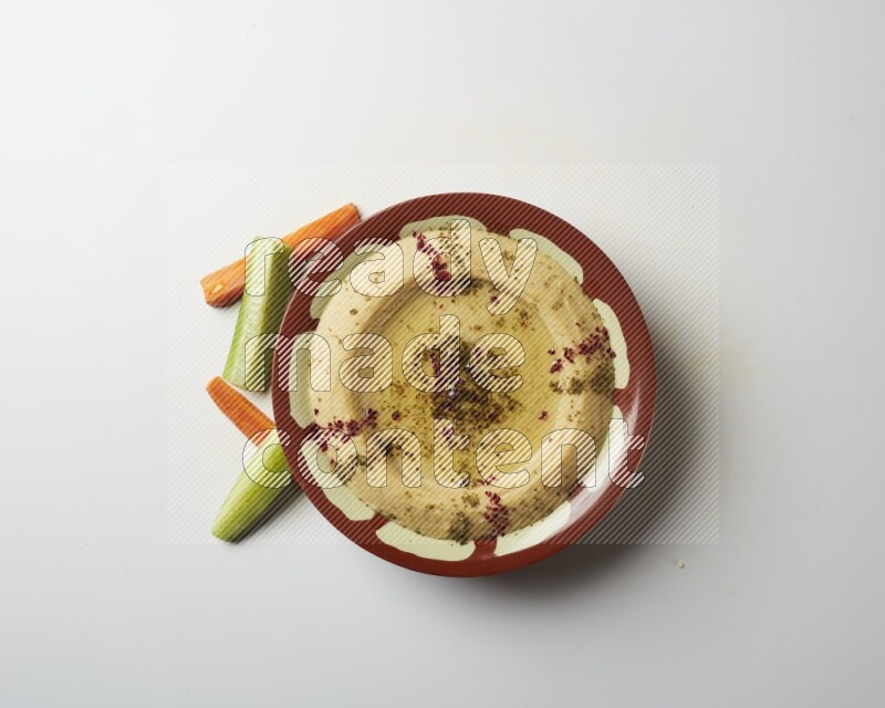 Hummus in a traditional plate garnished with zaatar & sumak on a white background
