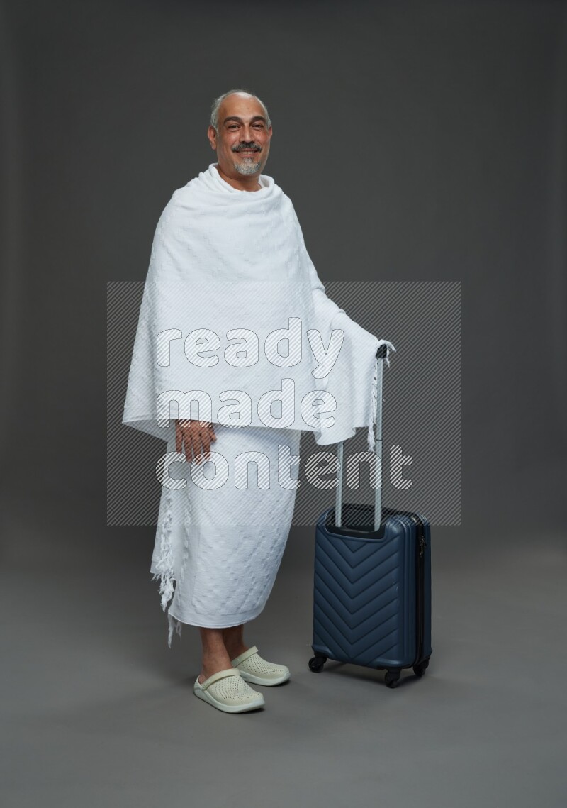 A man wearing Ehram Standing holding traveling bag on gray background