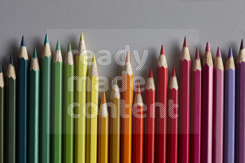 A collection of colored pencils arranged showcasing a gradient of different hues on grey background