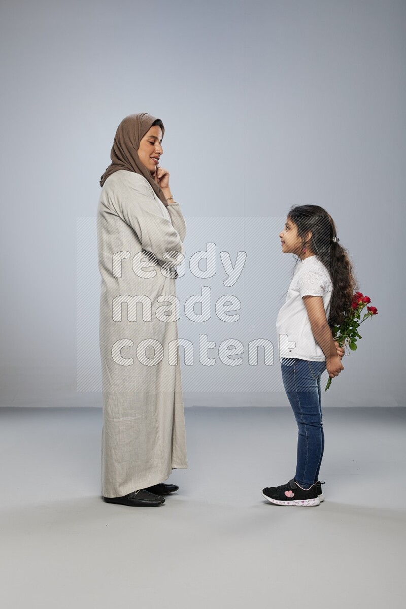 A girl standing giving flowers to her mother on gray background