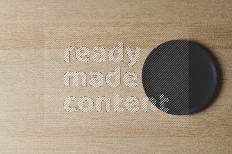 A black ceramic circular plate on light wooden background