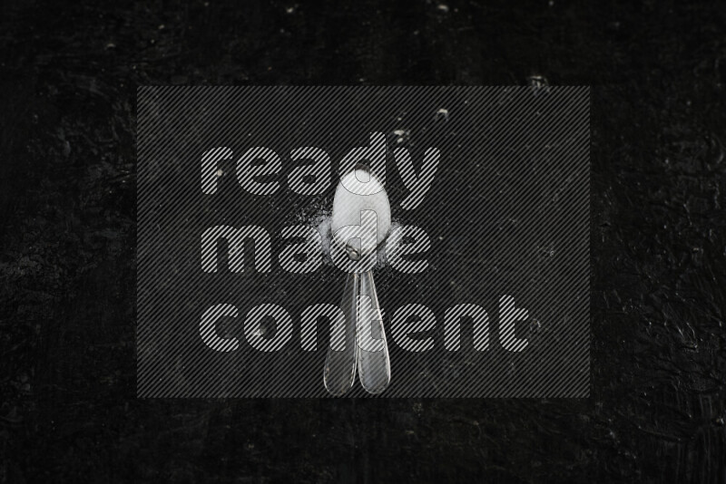 2 metal spoons filled with white salt on black background