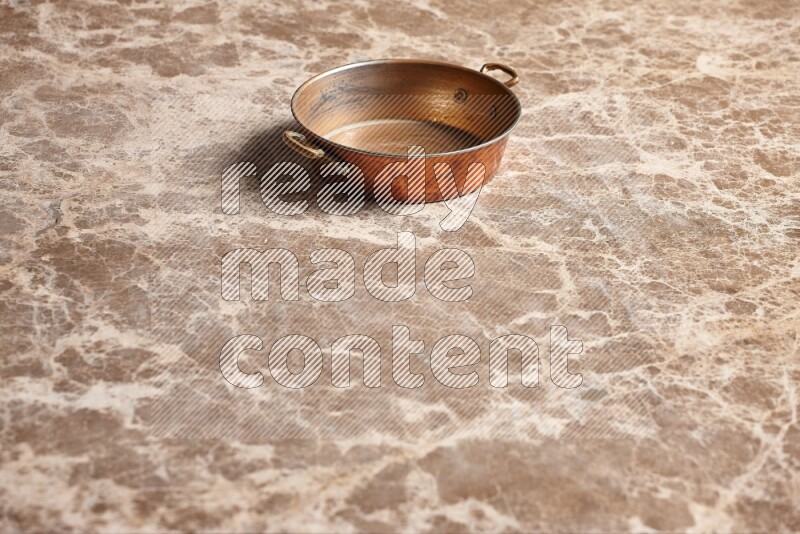 A small copper pan on beige marble background