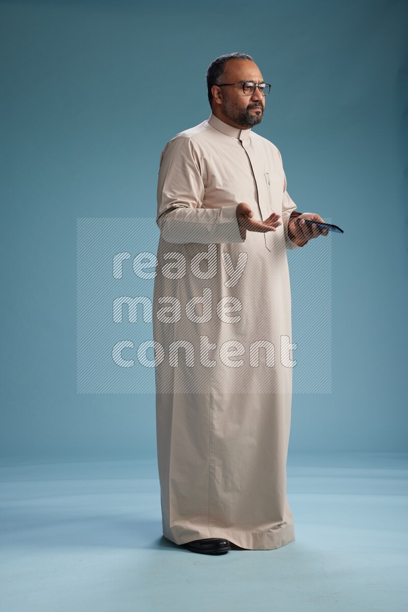 Saudi Man without shimag Standing texting on phone on blue background