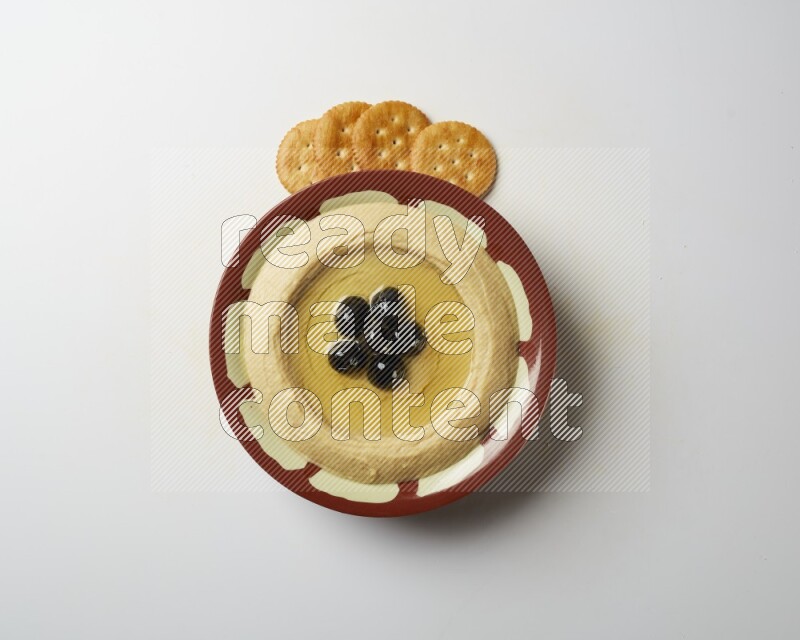 Hummus in a traditional plate garnished with black olives on a white background