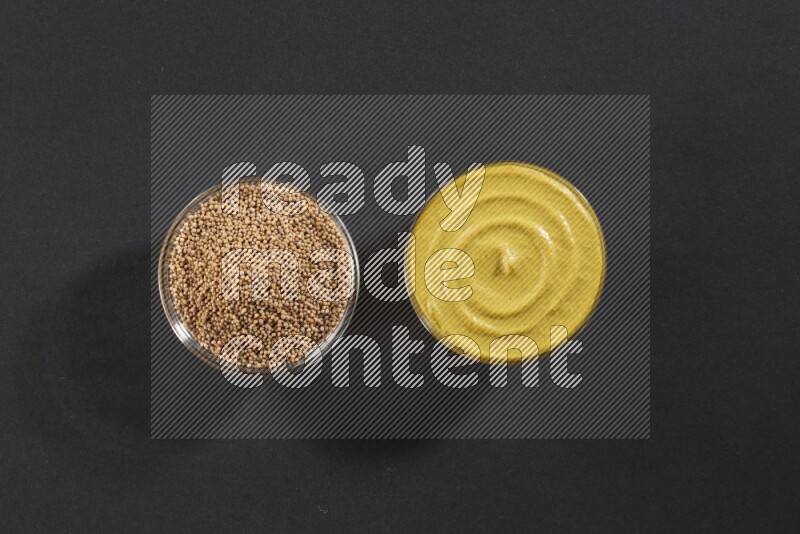 وعاءان زجاجيان إحداهما ممتلئ ببذور الخردل والأخر ممتلئ بمعجون الخردل علي خلفية سوداء