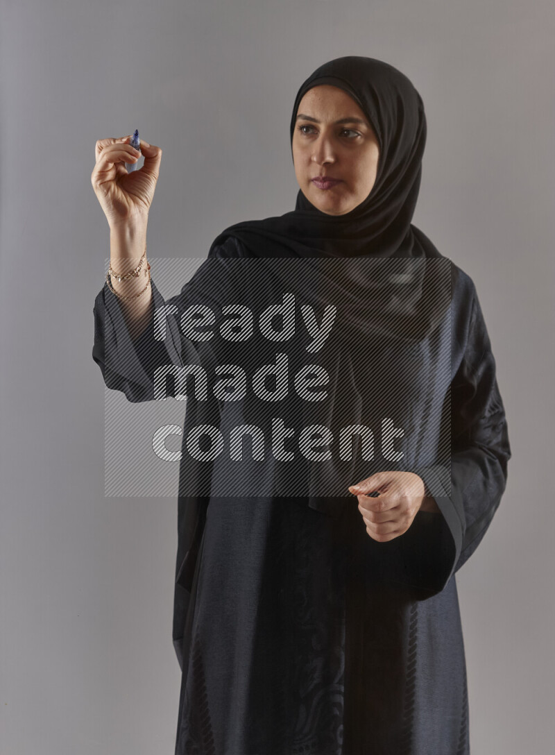 Woman in black abaya and hijab holding a marker pen to write on a transparent board with different reactions and expressions on grey background