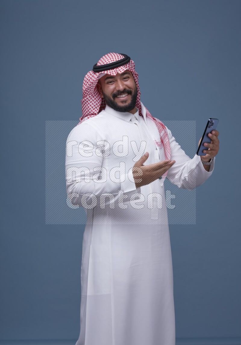 A man Texting on Blue Background wearing Saudi Thob and Shomag