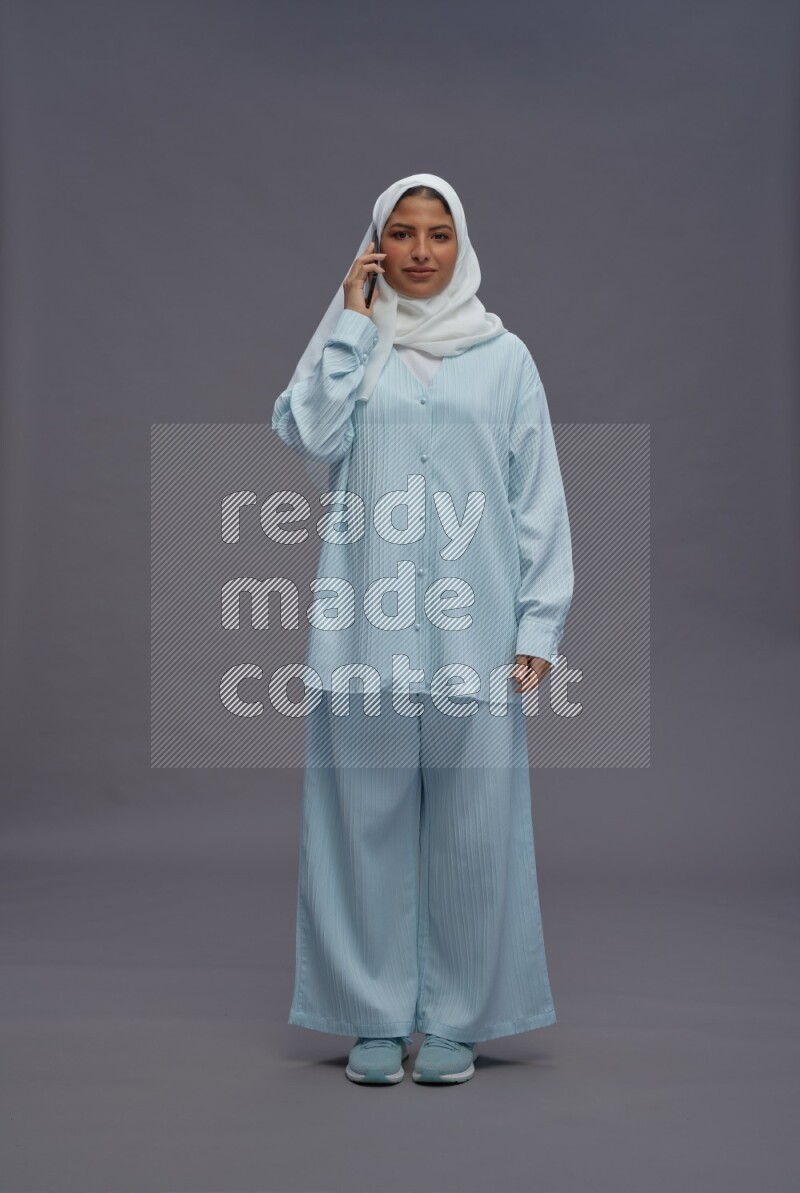 Saudi woman wearing hijab clothes standing talking on phone on gray background