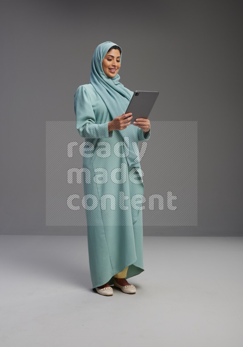 Saudi Woman wearing Abaya standing working on tablet on Gray background