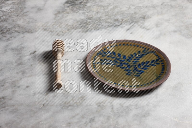 Decorative pottery plate with wooden honey dipper on the side on grey marble background