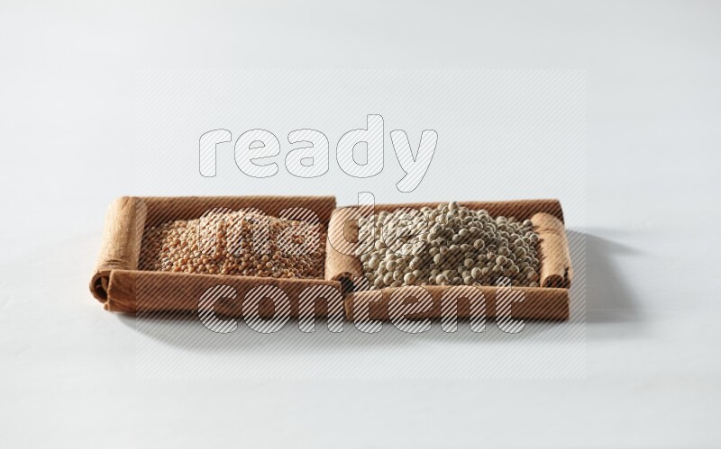 مربعان من أعواد القرفة ممتلئان بحبوب الخردل وحبوب الفلفل الأبيض علي خلفية بيضاء