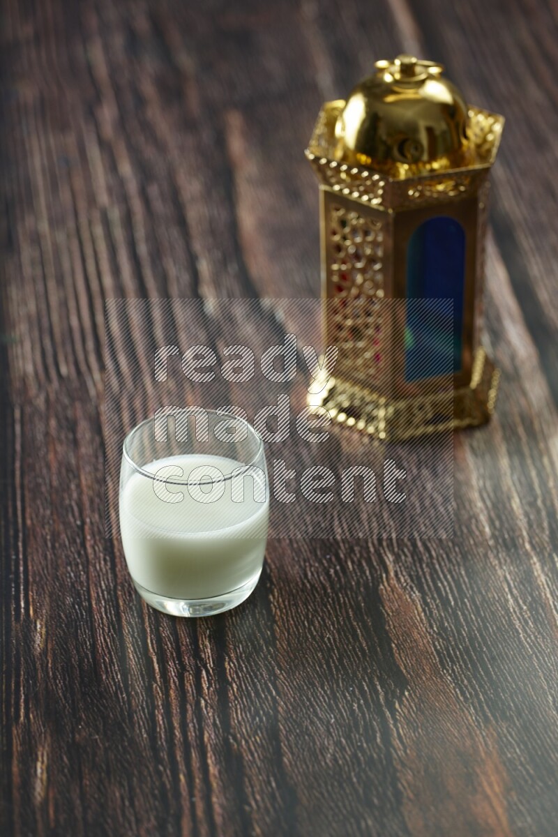 A golden lantern with different drinks, dates, nuts, prayer beads and quran on brown wooden background