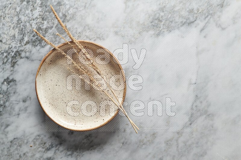 Wheat stalks on multicolored pottery plate on grey marble background