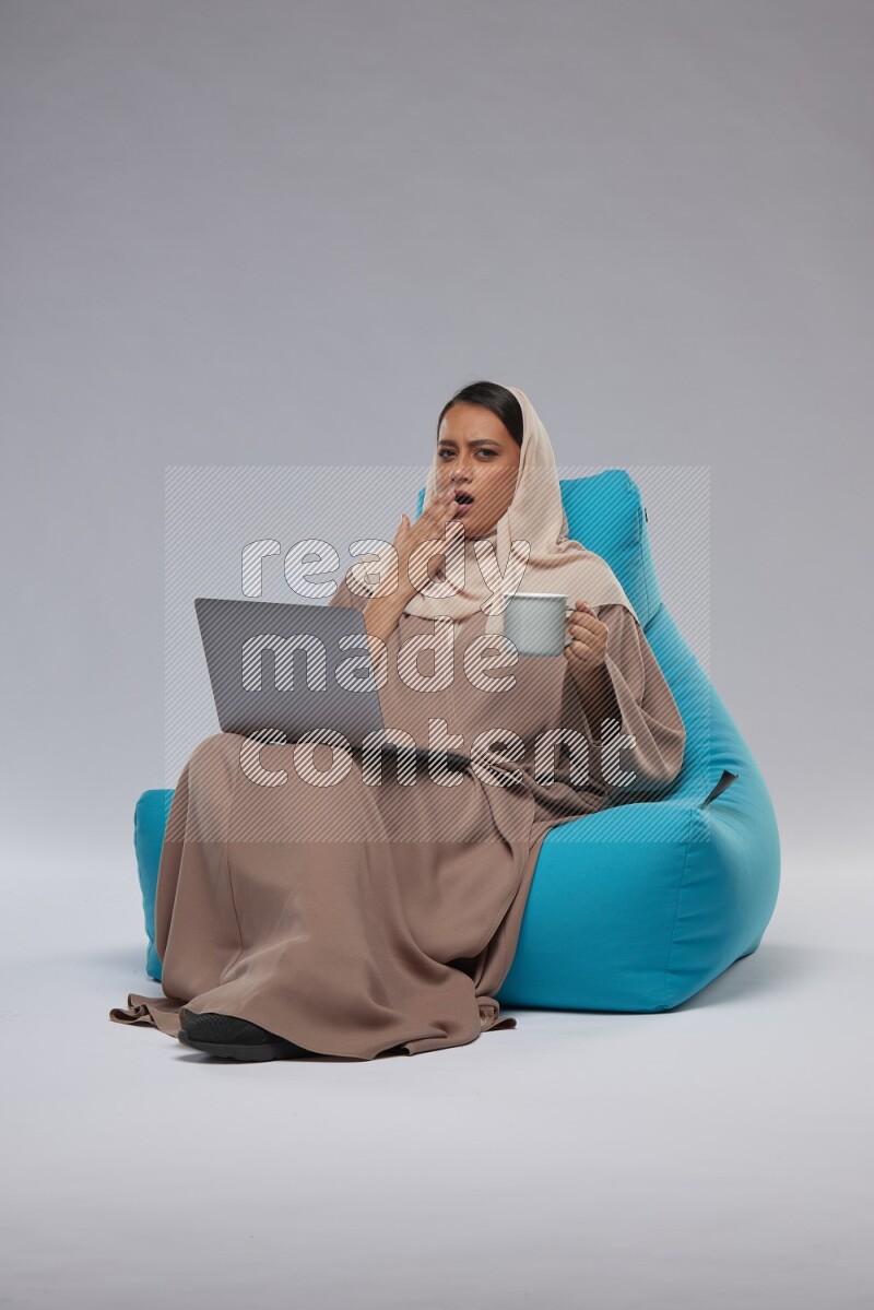 A Saudi woman sitting on a blue beanbag and working on laptop