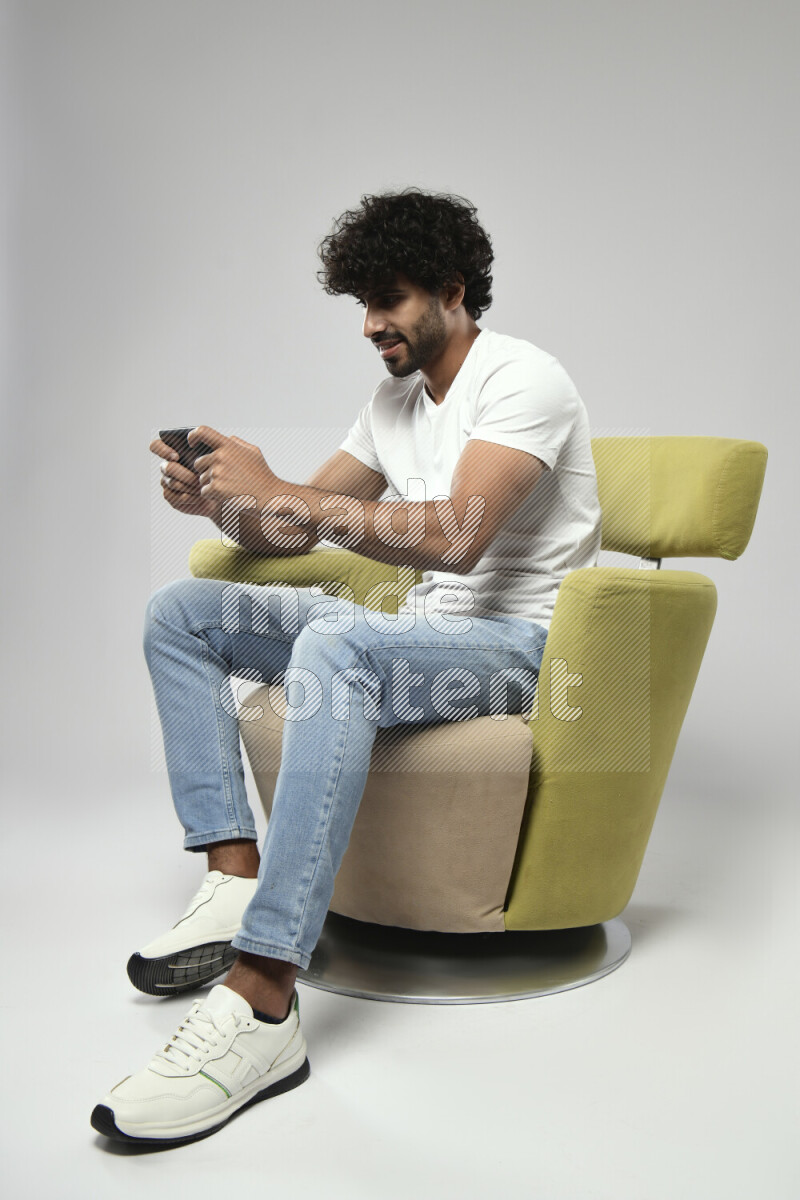 A man wearing casual sitting on a chair gaming on the phone on white background