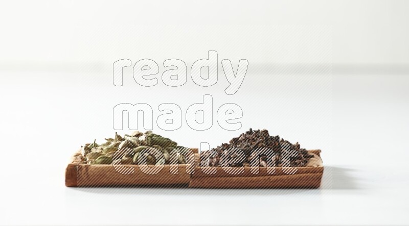 مربعان من أعواد القرفة ممتلئان بالقرنفل وحبوب الهيل علي خلفية بيضاء