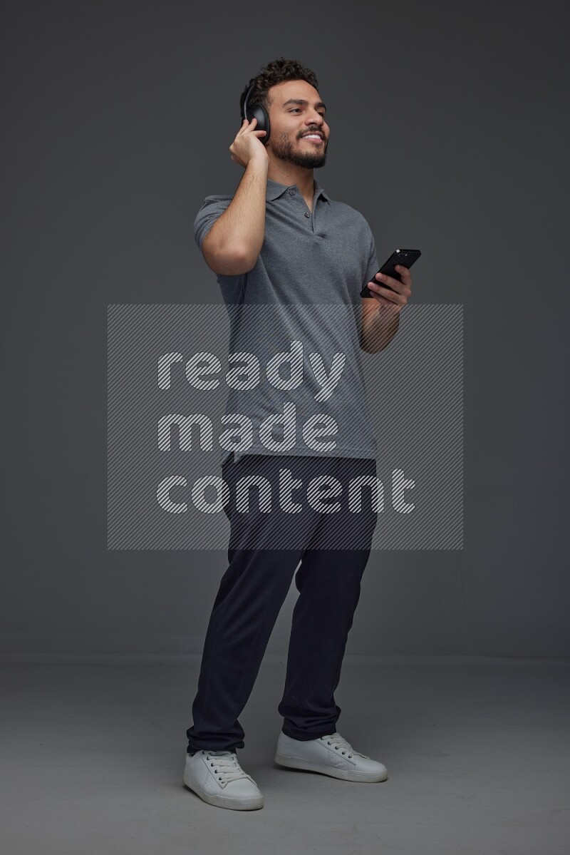 A man wearing casual and using his phone and headphone eye level on a gray background