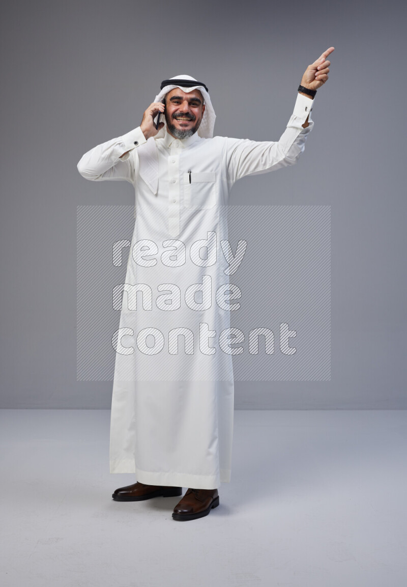 Saudi man Wearing Thob and white Shomag standing talking on phone on Gray background