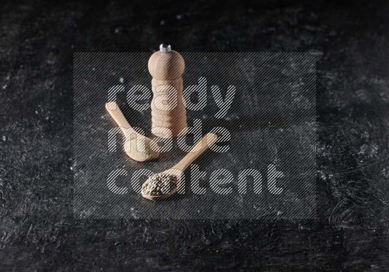 ملعقتان خشبيتان، واحدة ممتلئة ببودرة الفلفل الأبيض والأخرى بحبوب الفلفل ومطحنة خشبية على أرضية سوداء