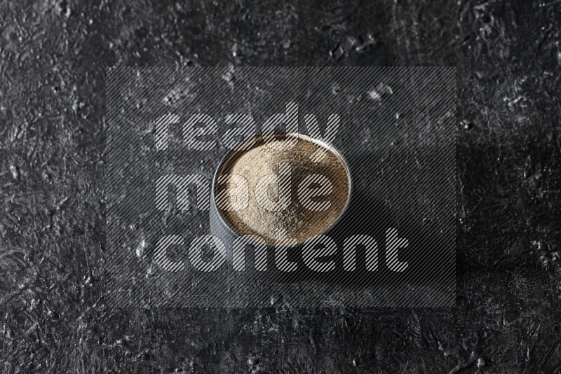 Black pottery bowl full of white pepper powder on textured black flooring