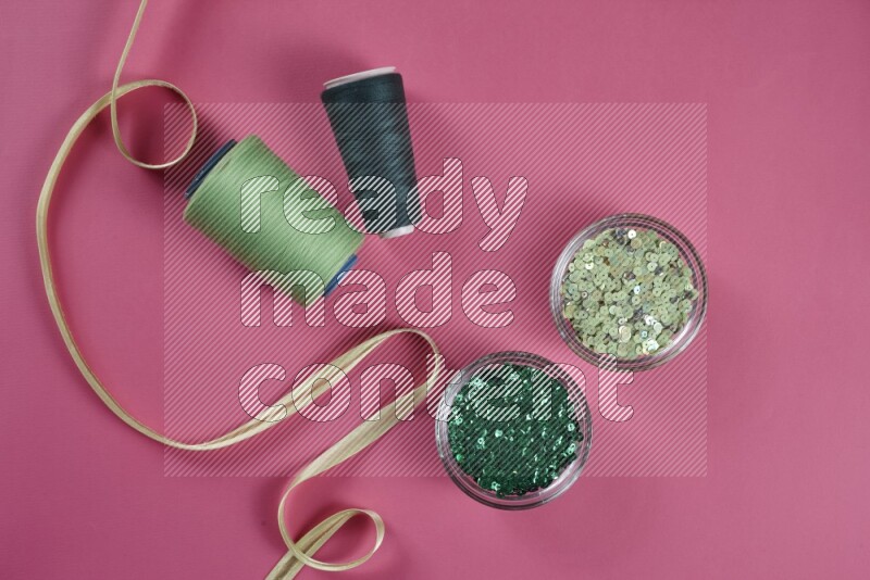 A green and pink collection of sewing and tailoring tools arranged on a pink background