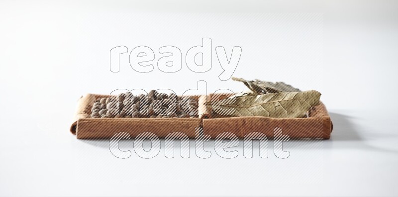 مربعان من أعواد القرفة ممتلئان ببهار الفلفل الحلو وأوراق الغار علي خلفية بيضاء