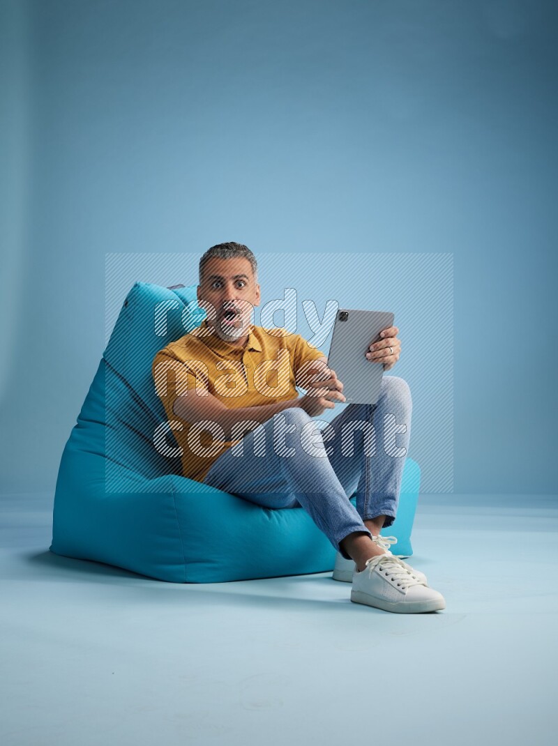 A man sitting on a blue beanbag and working on tablet