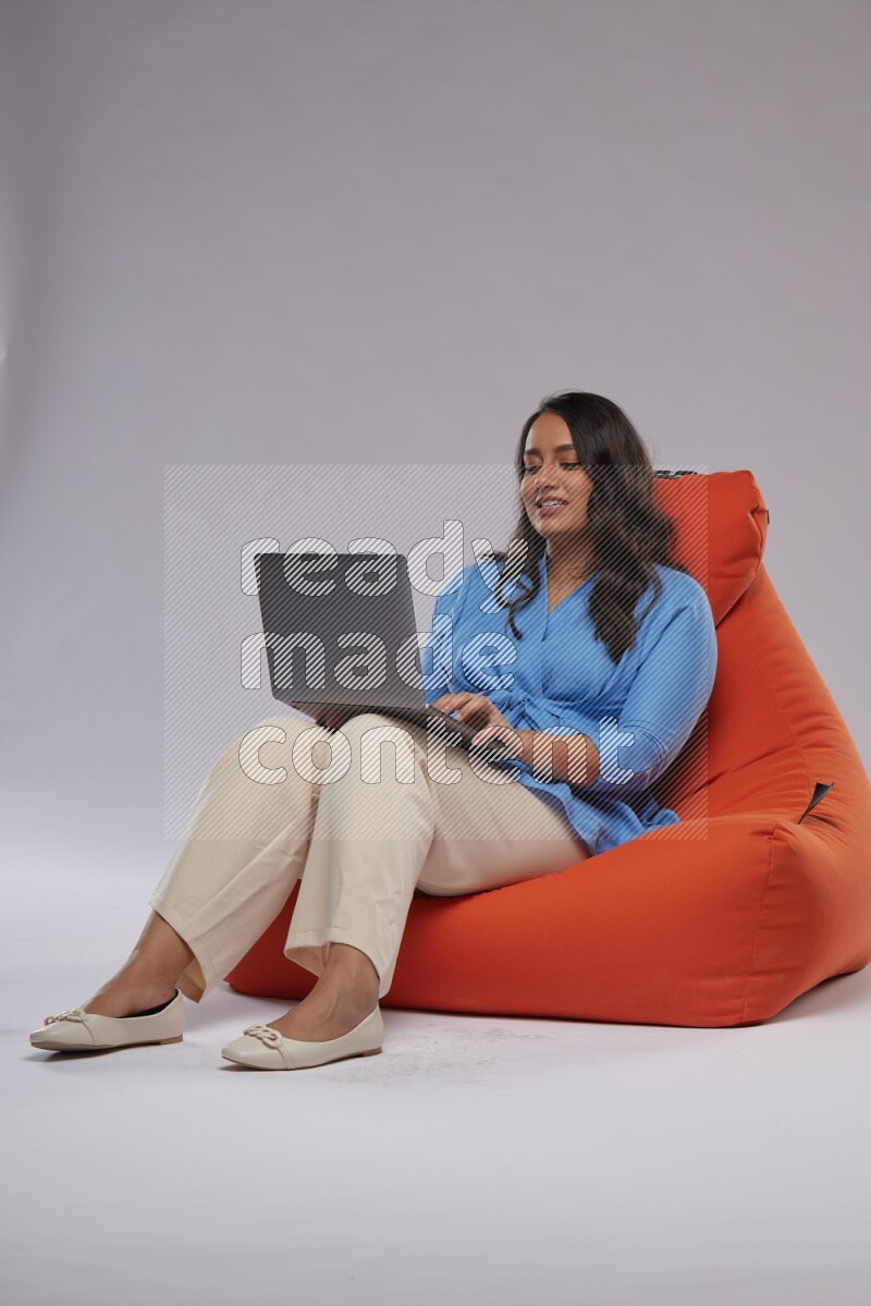 A woman sitting on an orange beanbag and working on laptop