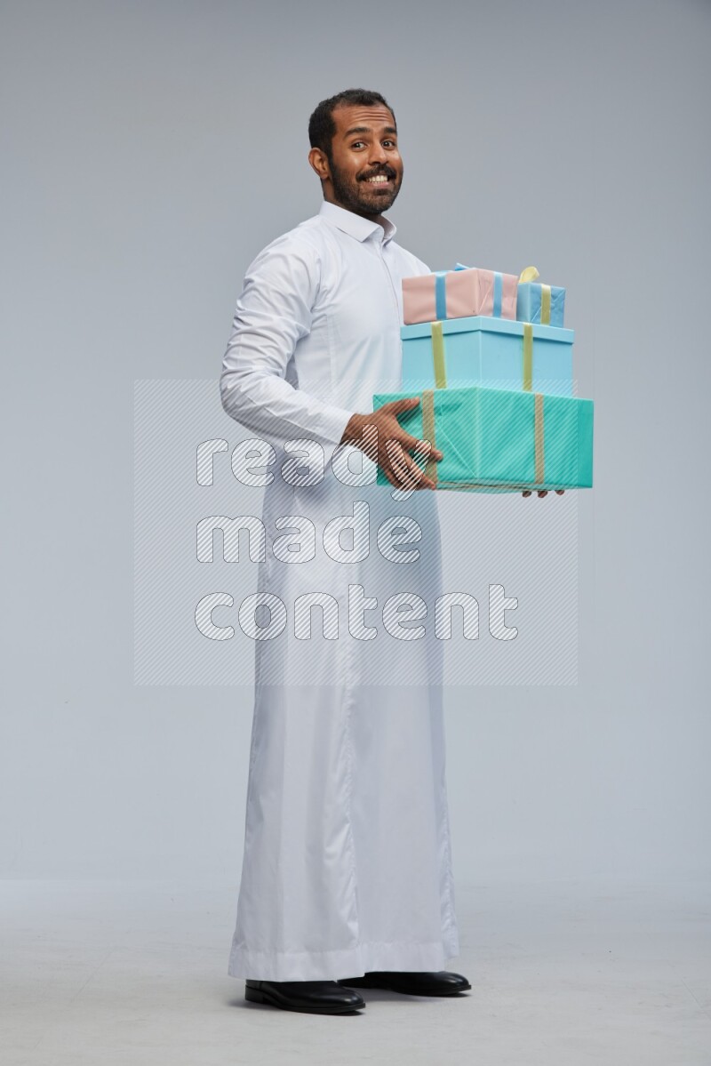 Saudi man Wearing thob standing holding gift box on Gray background