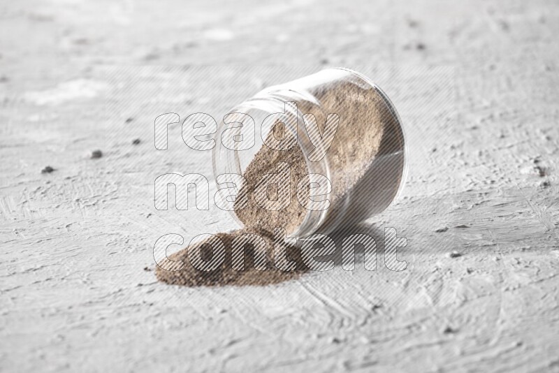 Flipped glass jar full of black pepper powder on a textured white flooring