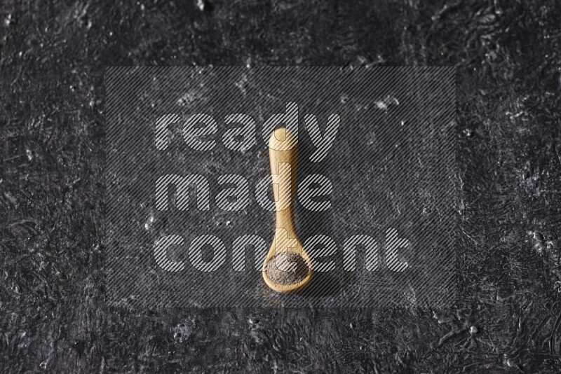 حبوب الفلفل الأسود في ملعقة خشبية علي خلفية سوداء