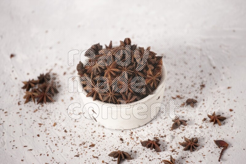 Star Anise in a white bowl and more of it sprinkled on white background
