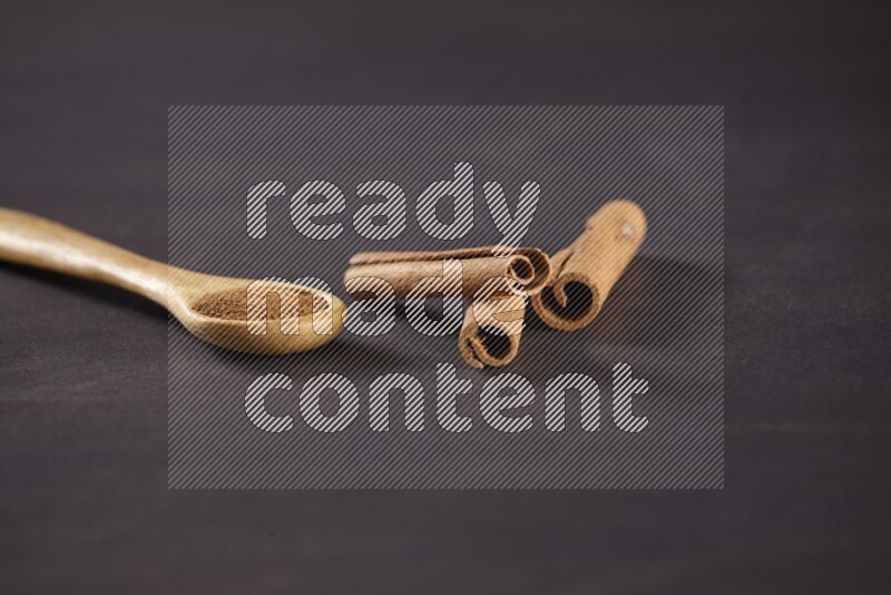 3 Cinnamon sticks stacked beside a wooden spoon full of cinnamon powder on black background in different angles
