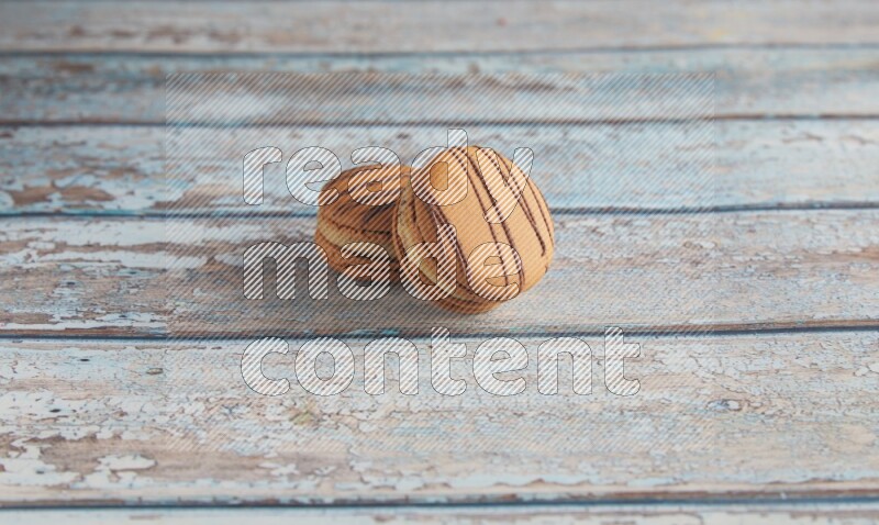 45º Shot of two light brown Almond Cream macarons on light blue wooden background