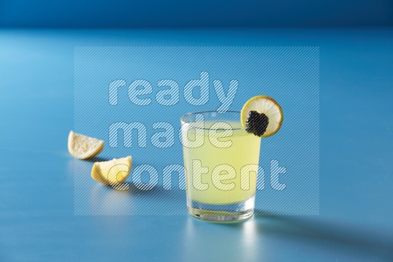 glass of lemon juice with lemon slice and berry on blue background