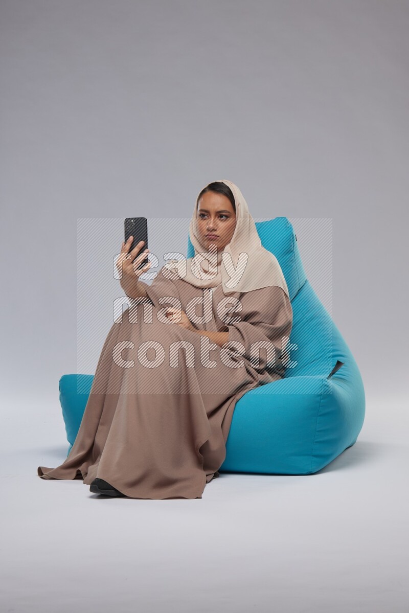 A Saudi woman sitting on a blue beanbag and taking selfie