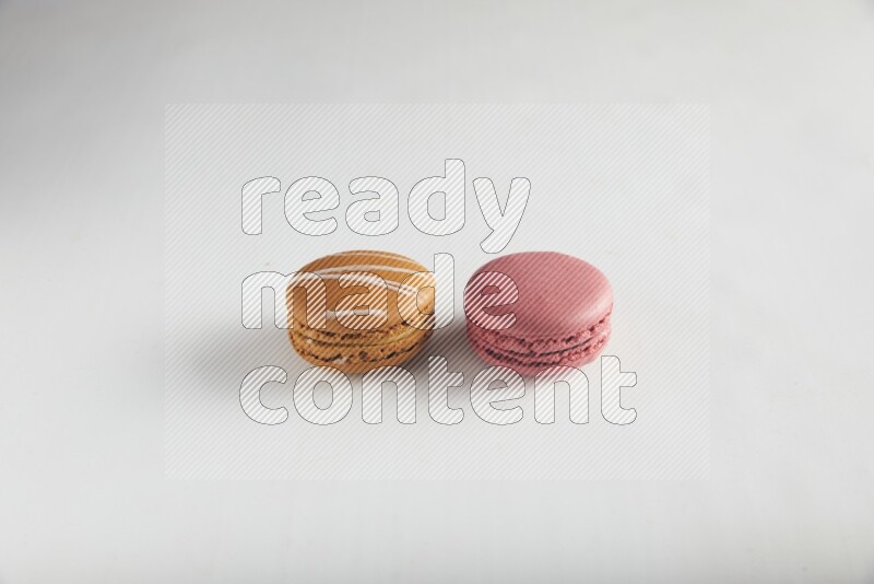 45º Shot of of two assorted Brown Irish Cream, and Pink Raspberry macarons on white background