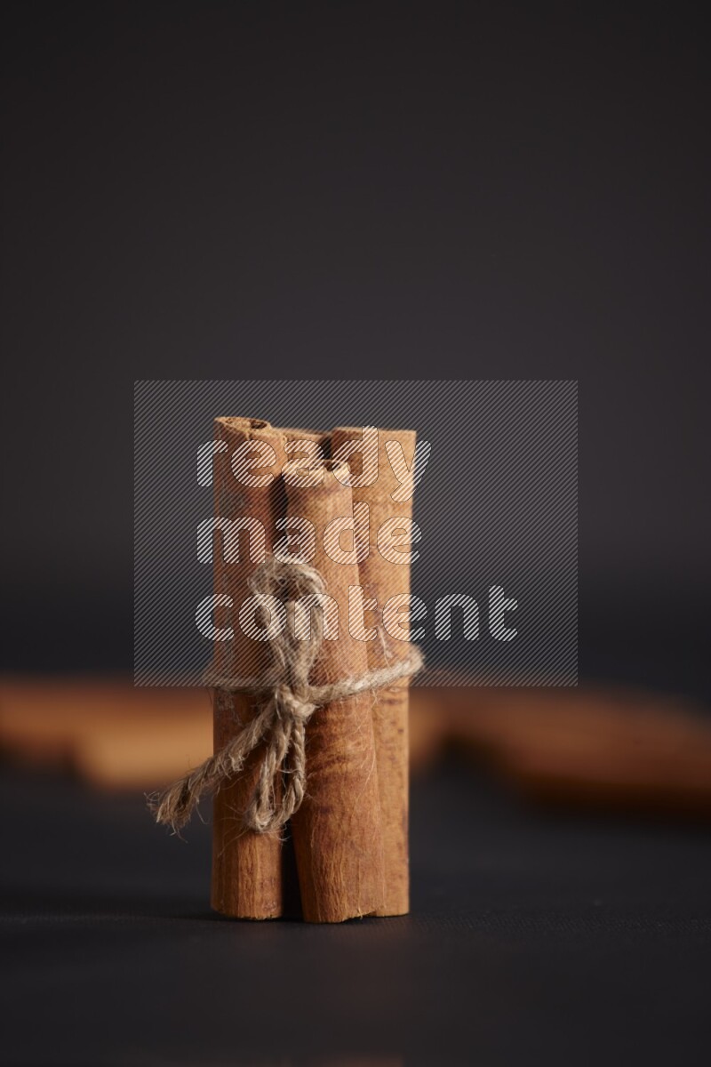 4 Cinnamon sticks stacked and bounded with more sticks in the background on black flooring