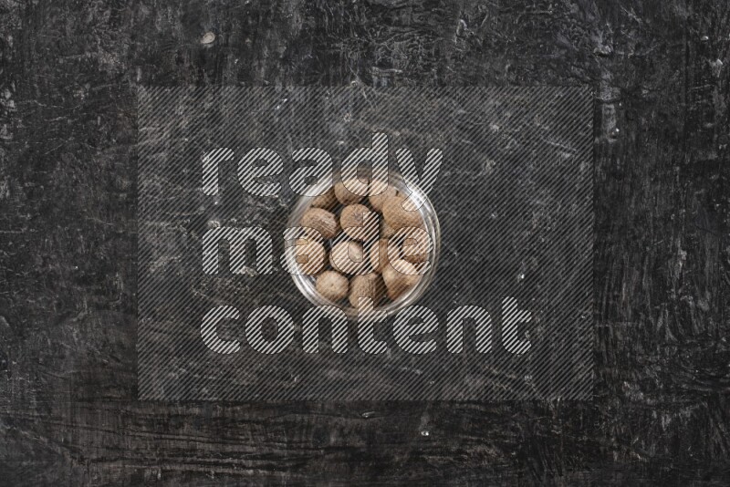 A glass jar full of whole nutmeg seeds on a black flooring