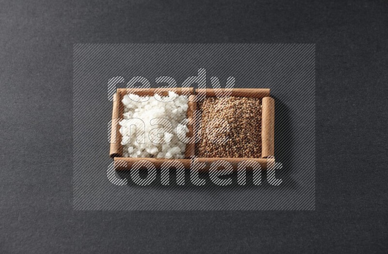 2 squares of cinnamon sticks full of mustard seeds and white salt on black flooring