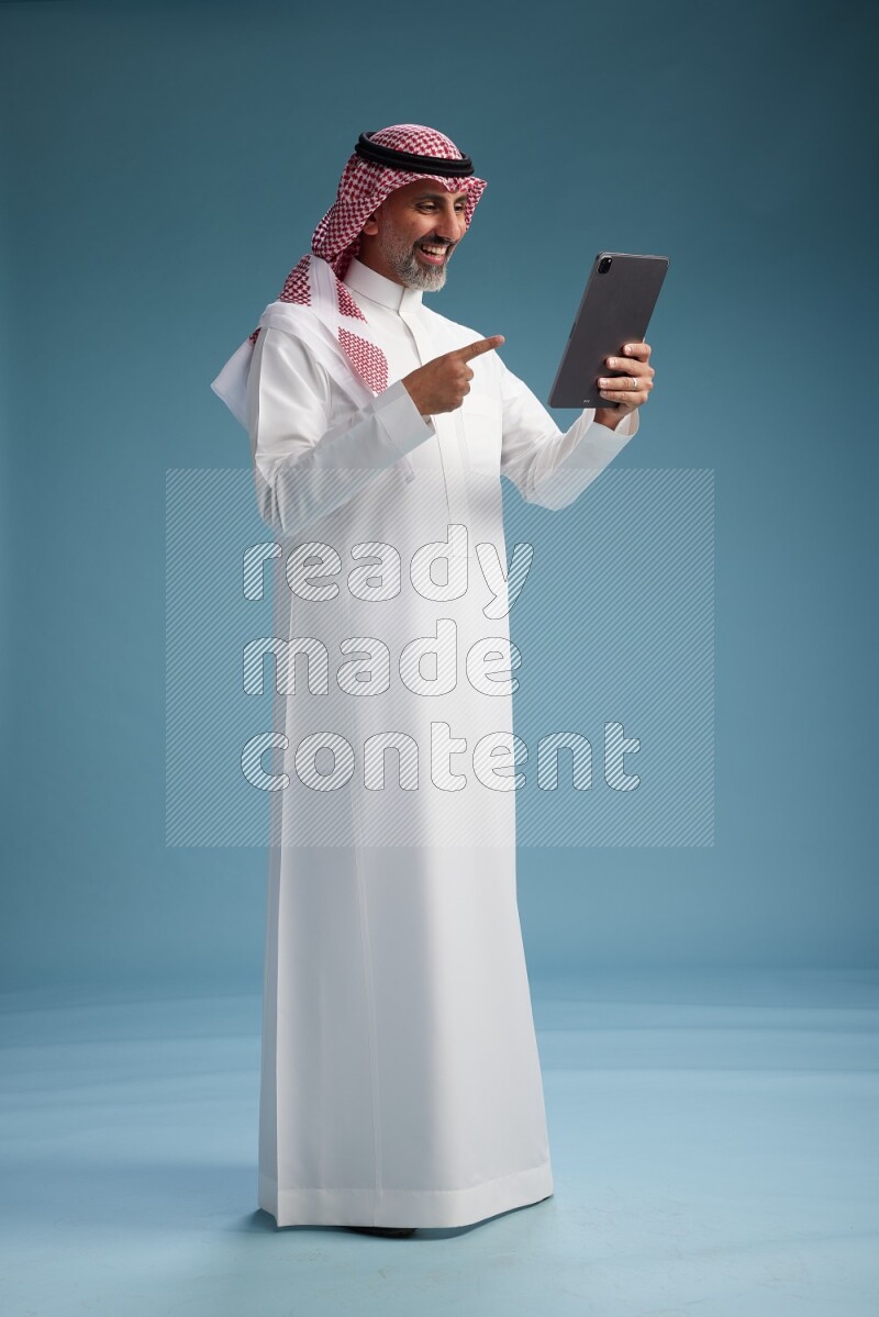 Saudi man wearing thob and shomagh with tablet on Blue background