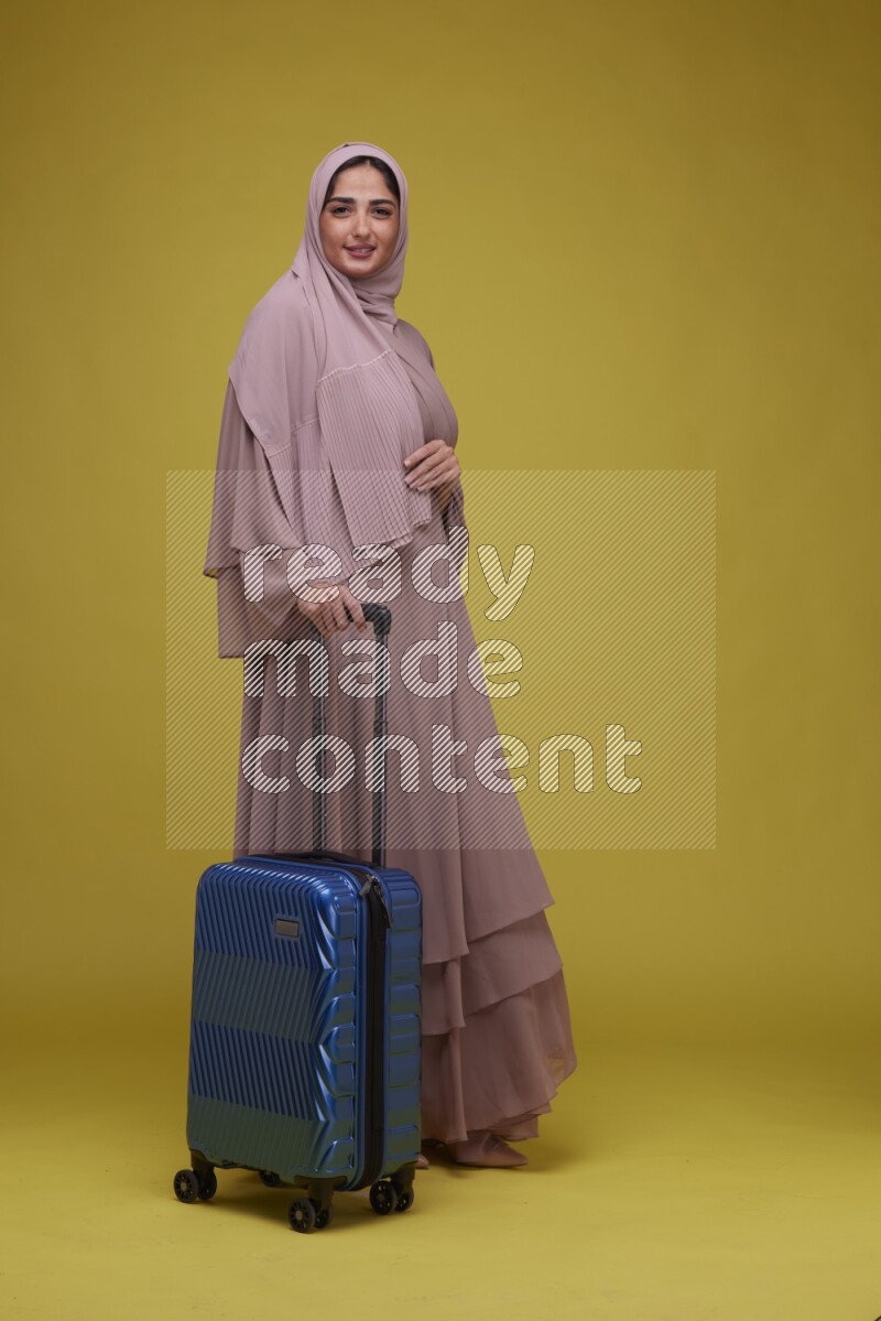 A woman With suit Case on a Yellow Background wearing Brown Abaya with Hijab