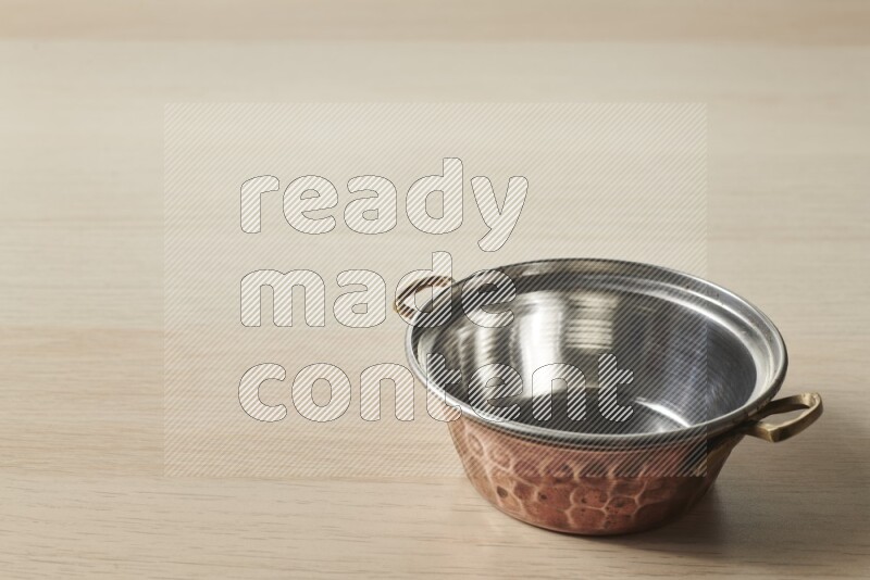 A small copper pot on light wooden background