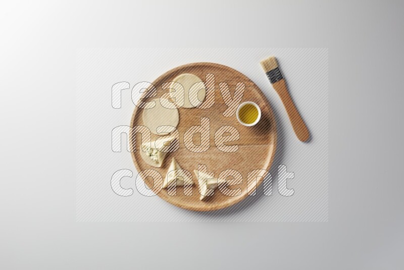 two closed sambosas and one open sambosa filled with cheese while oil with oil brush aside in a wooden dish on a white background