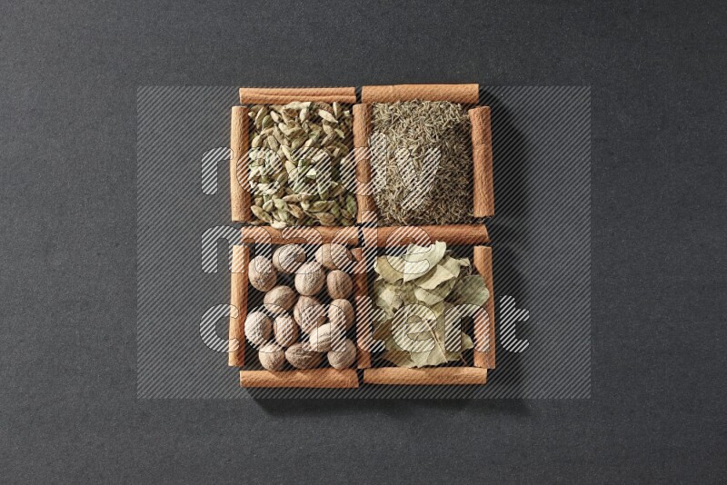 4 مربعات من عيدان القرفة ممتلئة بالكمون وحبوب الهيل وأوراق الغار وجوزة الطيب على أرضية سوداء