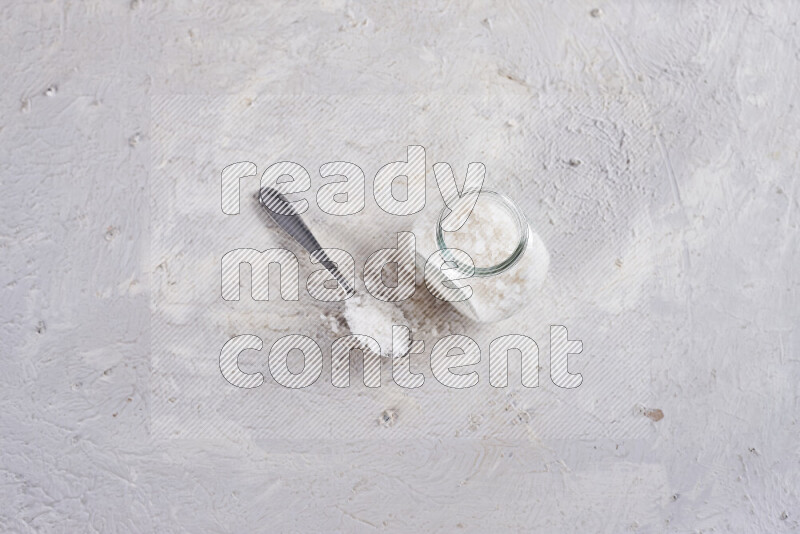 A glass jar full of coarse sea salt crystals on white background