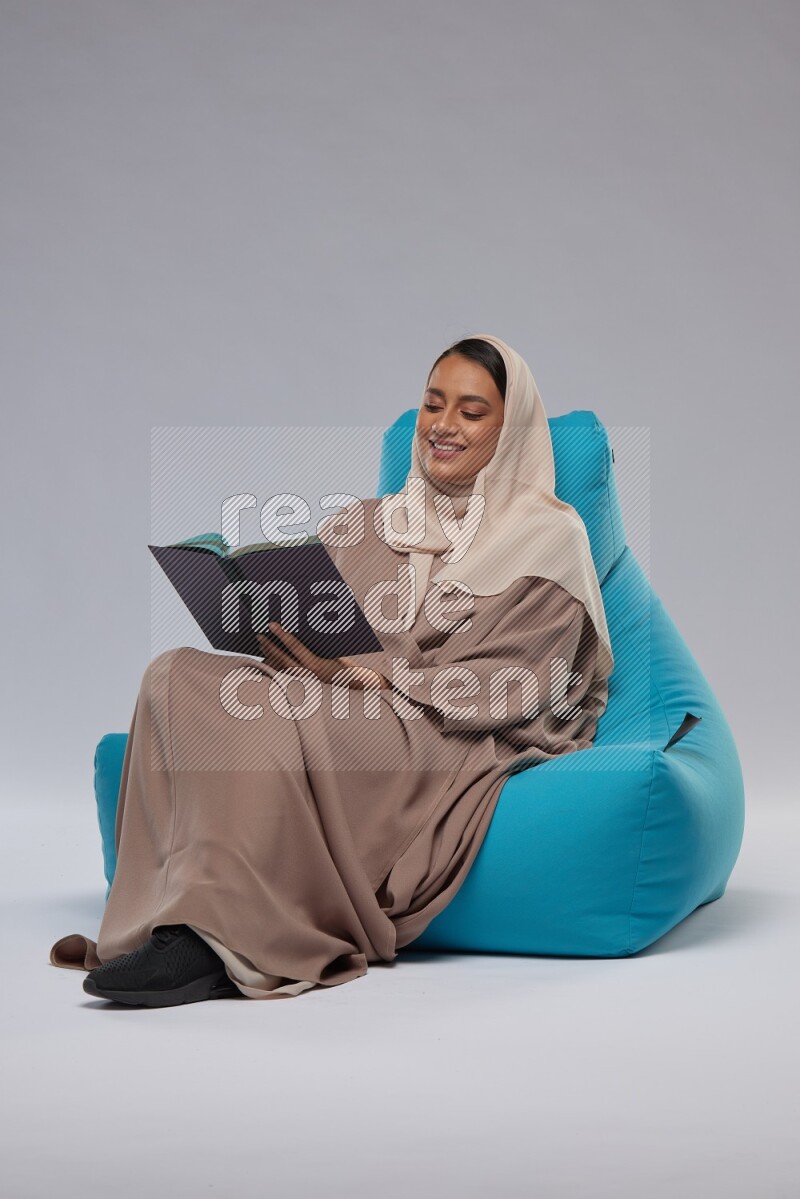 A woman sitting on a blue beanbag and reading a book