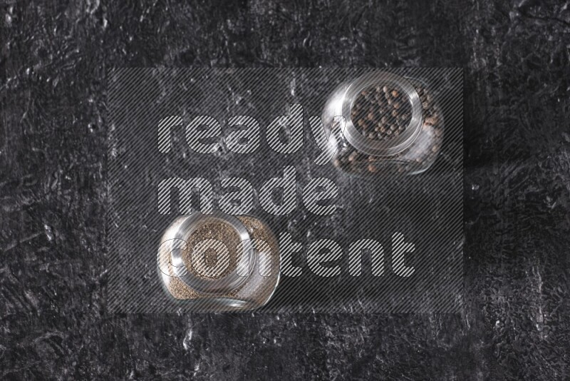 حبوب وبودرة الفلفل الأسود في أوعية زجاجية علي خلفية سوداء