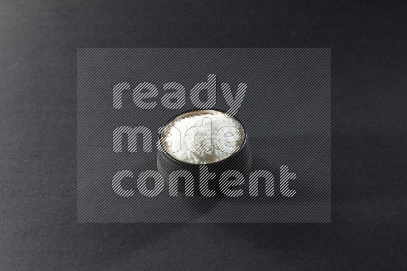 A black pottery bowl full of desiccated coconut on a black background in different angles